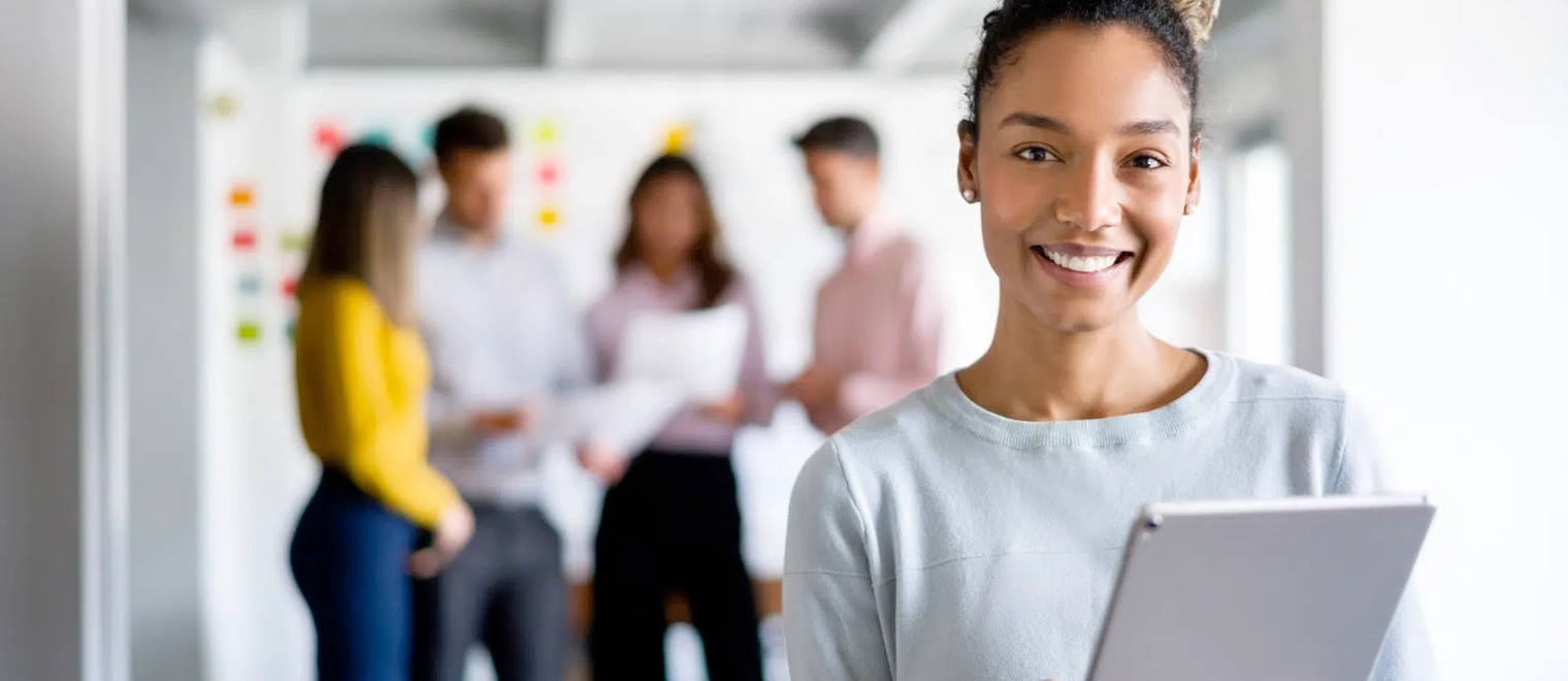 Smiling woman holding tablet in office setting.
